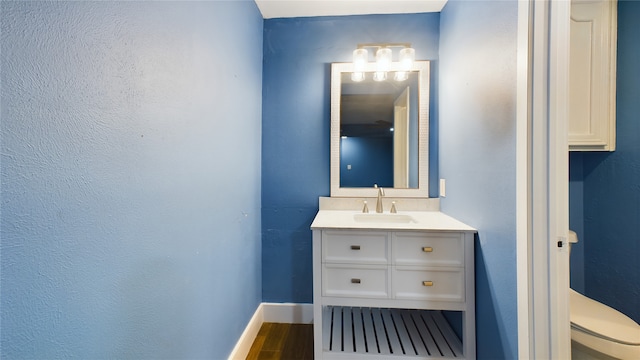 bathroom with toilet, wood finished floors, vanity, and baseboards