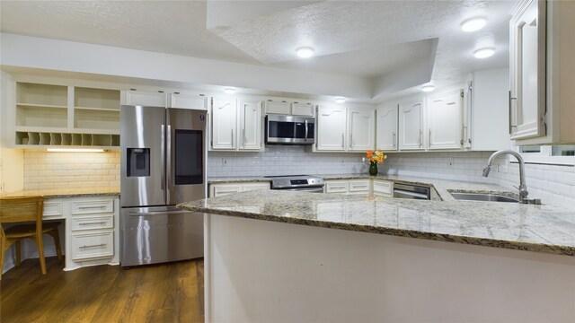 kitchen with tasteful backsplash, white cabinets, a sink, a peninsula, and stainless steel appliances