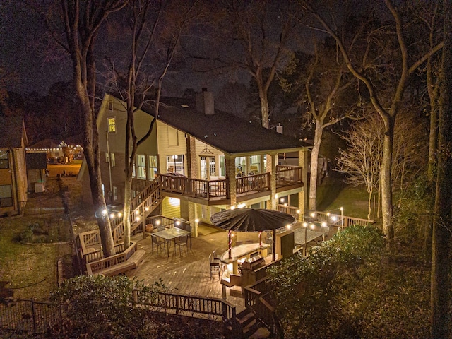 back of house at night featuring stairs, a deck, and a chimney