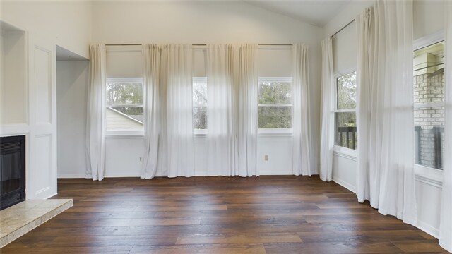 unfurnished living room with a healthy amount of sunlight, a fireplace with raised hearth, dark wood-style floors, and lofted ceiling