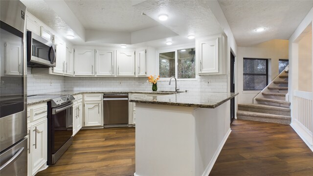 kitchen featuring appliances with stainless steel finishes, dark hardwood / wood-style flooring, sink, dark stone countertops, and white cabinetry