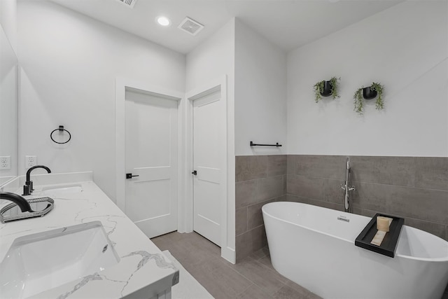 bathroom featuring tile patterned floors, vanity, a bath, and tile walls