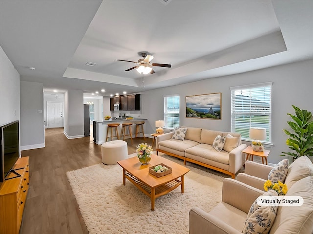 living room featuring hardwood / wood-style floors, ceiling fan, and a raised ceiling