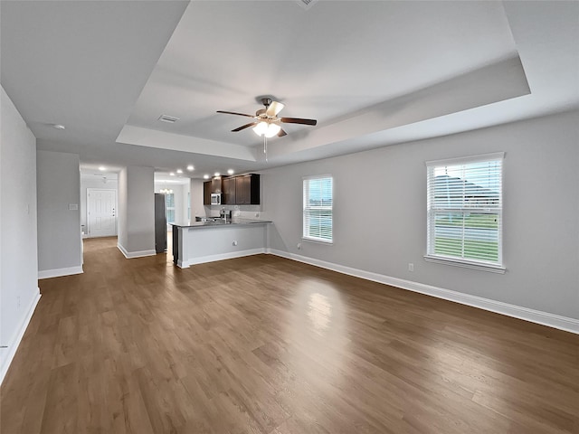 unfurnished living room featuring dark wood-type flooring, a raised ceiling, and a healthy amount of sunlight