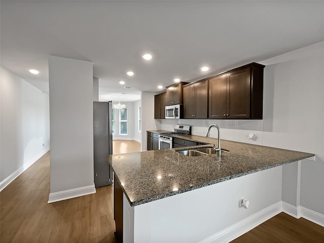 kitchen with sink, hardwood / wood-style flooring, dark brown cabinetry, kitchen peninsula, and stainless steel appliances