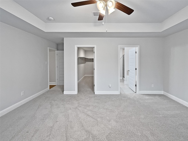 unfurnished bedroom featuring light carpet, ensuite bath, ceiling fan, a spacious closet, and a closet