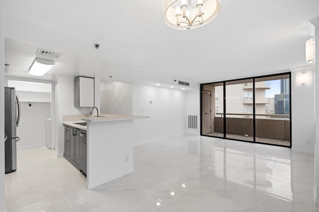 kitchen featuring appliances with stainless steel finishes, sink, a wall of windows, a notable chandelier, and white cabinets