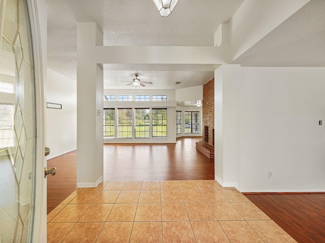 interior space featuring ceiling fan, light hardwood / wood-style floors, a textured ceiling, and a brick fireplace