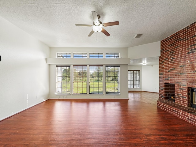 unfurnished living room with a textured ceiling, hardwood / wood-style flooring, a brick fireplace, and ceiling fan