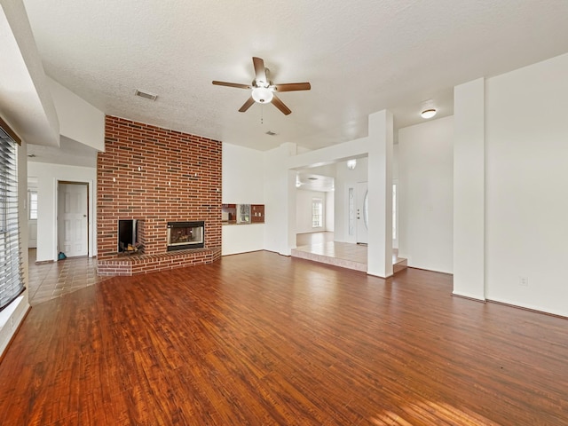 unfurnished living room featuring a textured ceiling, a brick fireplace, ceiling fan, and dark wood-type flooring