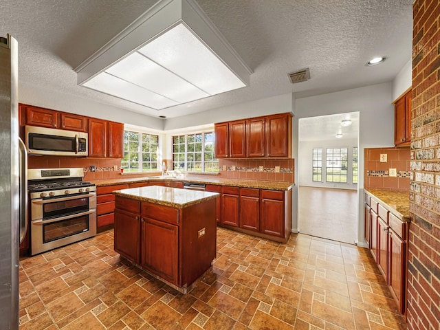 kitchen featuring light stone countertops, appliances with stainless steel finishes, backsplash, a textured ceiling, and a kitchen island