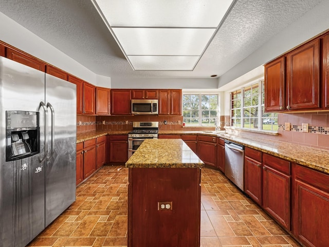 kitchen with light stone countertops, a center island, backsplash, a textured ceiling, and appliances with stainless steel finishes