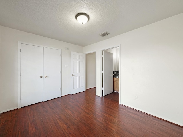 unfurnished bedroom with a textured ceiling, a closet, and dark hardwood / wood-style floors