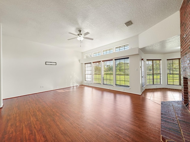 unfurnished room featuring hardwood / wood-style flooring, ceiling fan, a textured ceiling, and a brick fireplace