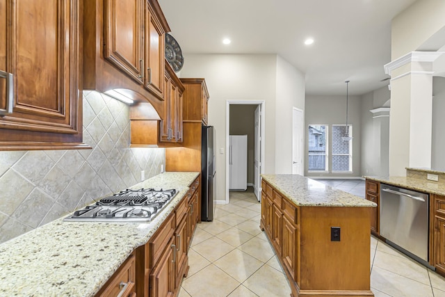 kitchen with pendant lighting, decorative backsplash, light stone countertops, a kitchen island, and stainless steel appliances