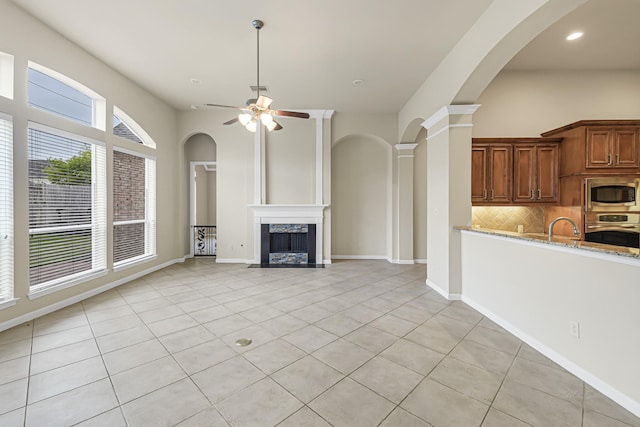 unfurnished living room featuring ceiling fan, sink, light tile patterned floors, and a fireplace