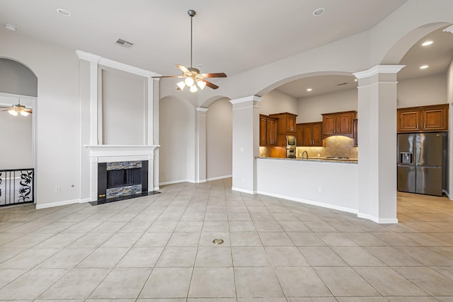 unfurnished living room featuring decorative columns, ceiling fan, a high end fireplace, and light tile patterned flooring