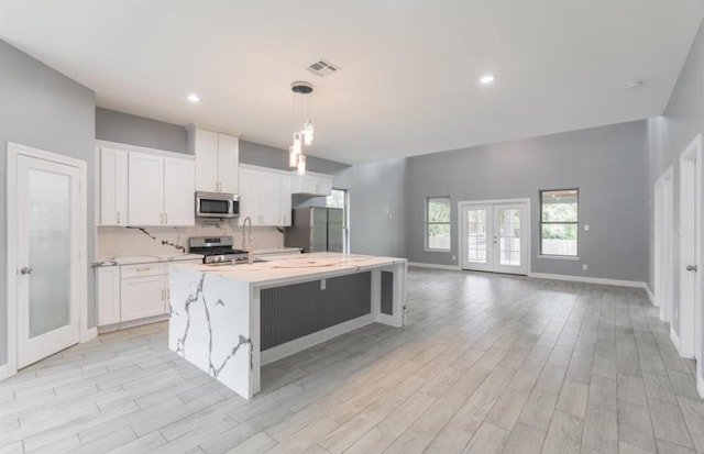 kitchen with appliances with stainless steel finishes, light wood-type flooring, decorative light fixtures, and white cabinetry