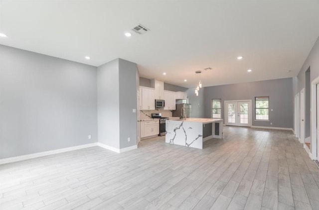 kitchen featuring light wood-type flooring, stainless steel appliances, a kitchen island with sink, pendant lighting, and white cabinetry