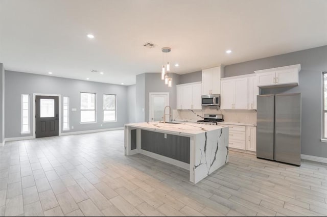 kitchen with appliances with stainless steel finishes, a kitchen island with sink, light hardwood / wood-style flooring, white cabinetry, and hanging light fixtures