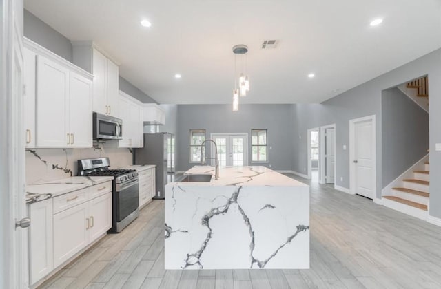 kitchen featuring white cabinets, decorative light fixtures, a center island with sink, and stainless steel appliances