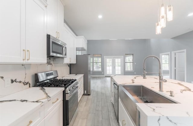 kitchen featuring decorative light fixtures, stainless steel appliances, white cabinetry, and light hardwood / wood-style flooring