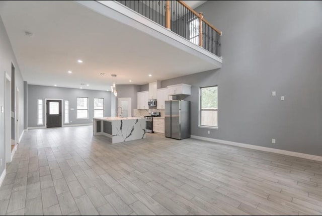 kitchen with white cabinets, a kitchen breakfast bar, light wood-type flooring, an island with sink, and stainless steel appliances