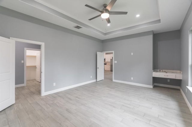 unfurnished bedroom featuring a raised ceiling, light wood-type flooring, a spacious closet, and ceiling fan