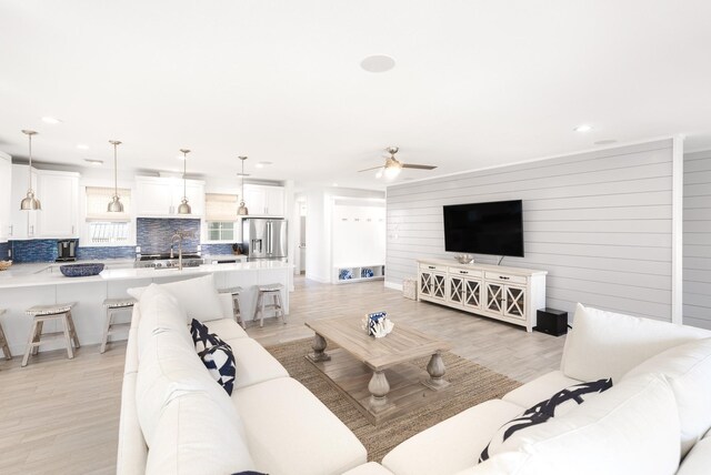 living room featuring ceiling fan, sink, light hardwood / wood-style floors, and wood walls