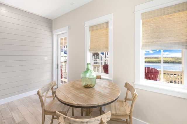 dining room with a water view, wood walls, baseboards, and wood finished floors