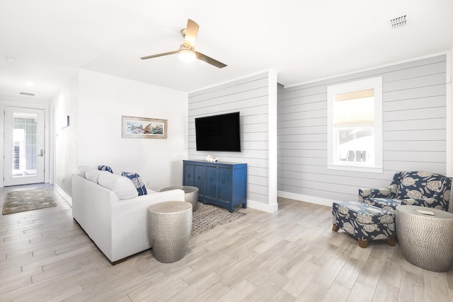 living room with light wood-type flooring, baseboards, ceiling fan, and visible vents