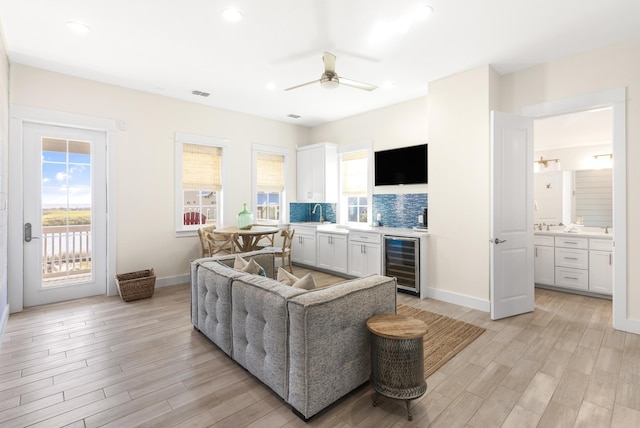 living area featuring light wood finished floors, beverage cooler, baseboards, ceiling fan, and recessed lighting