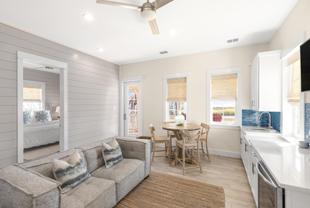 living room featuring wooden walls, sink, wine cooler, ceiling fan, and light wood-type flooring