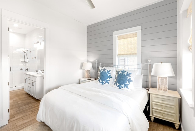 bedroom with hardwood / wood-style flooring, wooden walls, connected bathroom, and ceiling fan