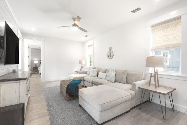 living area featuring baseboards, visible vents, light wood-style floors, and a ceiling fan