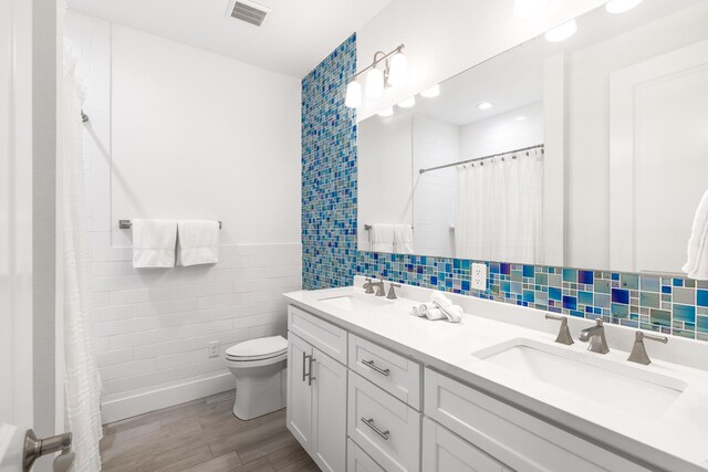 bathroom featuring tile walls, hardwood / wood-style flooring, vanity, toilet, and a shower with curtain