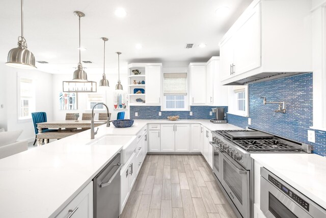 kitchen with light countertops, stainless steel appliances, white cabinetry, a sink, and pendant lighting