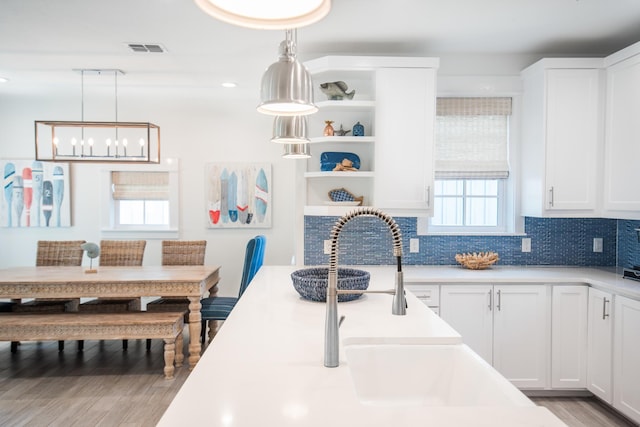 kitchen featuring white cabinetry, backsplash, light wood-type flooring, and pendant lighting