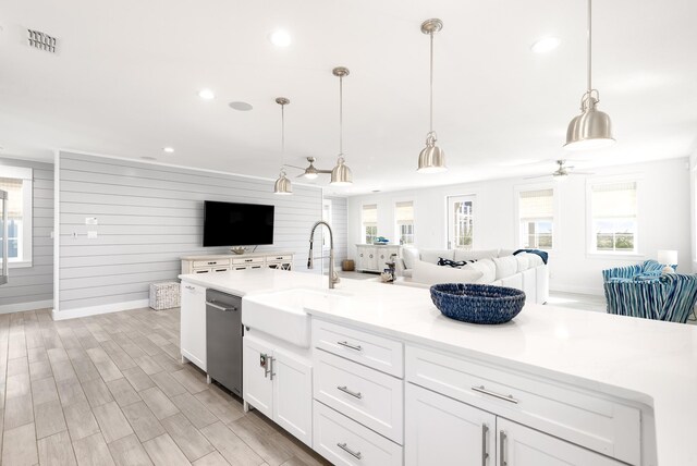 kitchen featuring sink, white cabinetry, hanging light fixtures, wooden walls, and light wood-type flooring