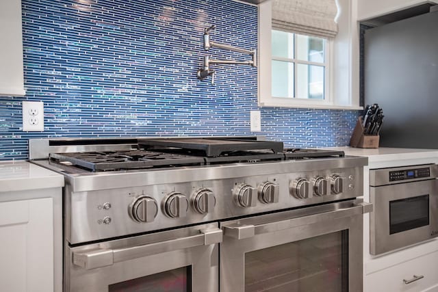 kitchen featuring decorative backsplash, light countertops, appliances with stainless steel finishes, glass insert cabinets, and white cabinetry