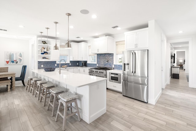 kitchen featuring a sink, open shelves, a kitchen breakfast bar, appliances with stainless steel finishes, and a peninsula