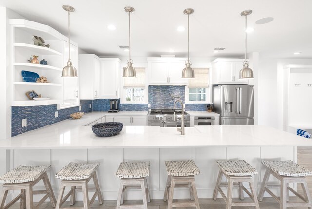 kitchen with high end appliances, hanging light fixtures, a kitchen breakfast bar, decorative backsplash, and white cabinets