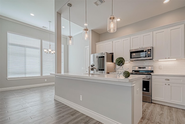 kitchen with appliances with stainless steel finishes, a center island with sink, white cabinetry, and hanging light fixtures