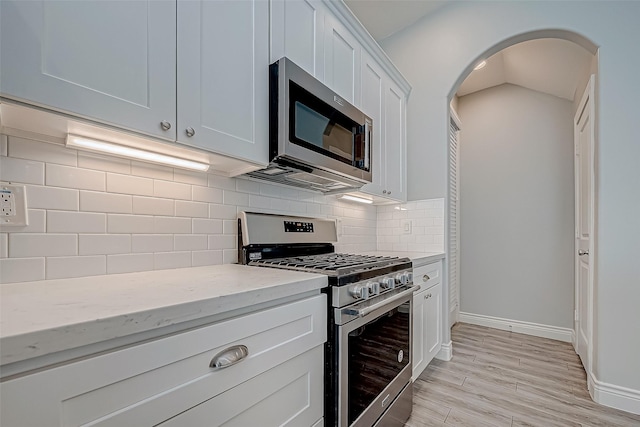 kitchen with decorative backsplash, light stone countertops, light wood-type flooring, stainless steel appliances, and white cabinets