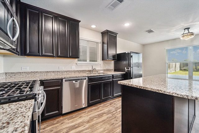 kitchen featuring light wood-type flooring, appliances with stainless steel finishes, light stone counters, and sink