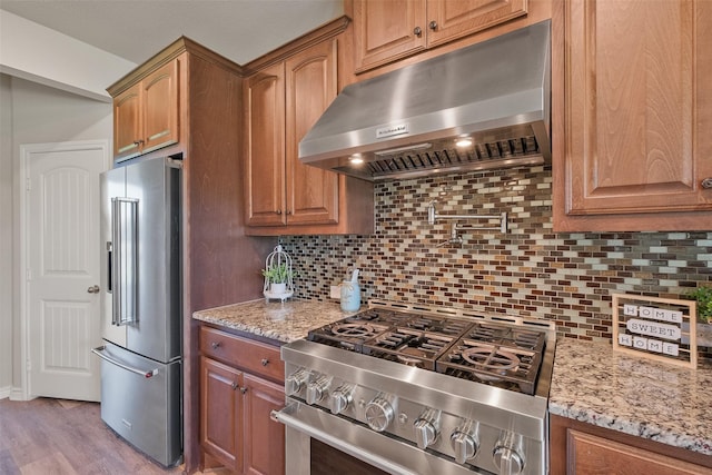 kitchen with light wood-type flooring, premium appliances, tasteful backsplash, and light stone counters