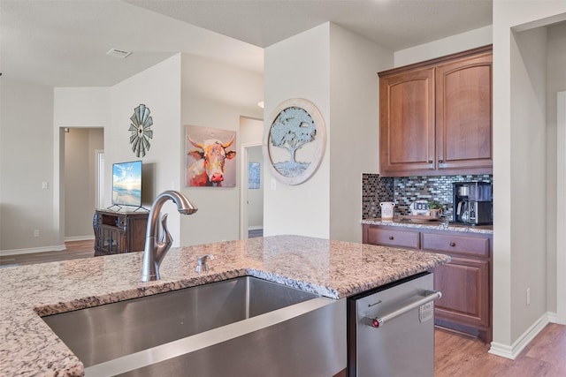 kitchen featuring sink, stainless steel dishwasher, light stone countertops, tasteful backsplash, and light hardwood / wood-style floors