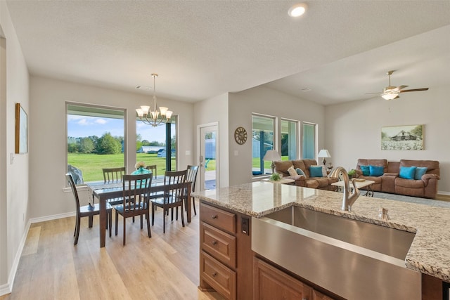 kitchen with ceiling fan with notable chandelier, sink, light stone countertops, decorative light fixtures, and light hardwood / wood-style floors