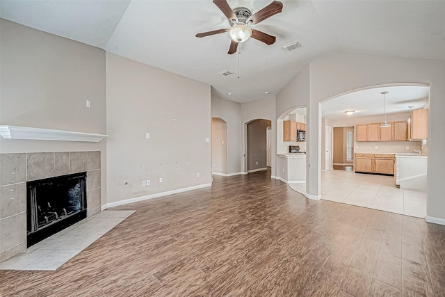 unfurnished living room with a fireplace, light wood-type flooring, ceiling fan, and lofted ceiling