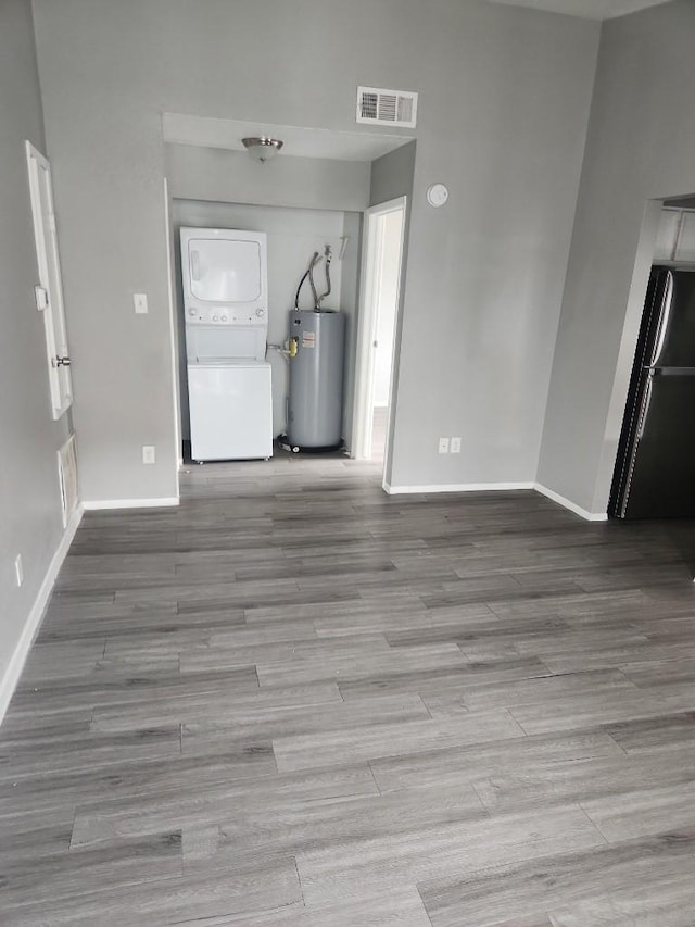 unfurnished living room with stacked washer / dryer, electric water heater, and light wood-type flooring